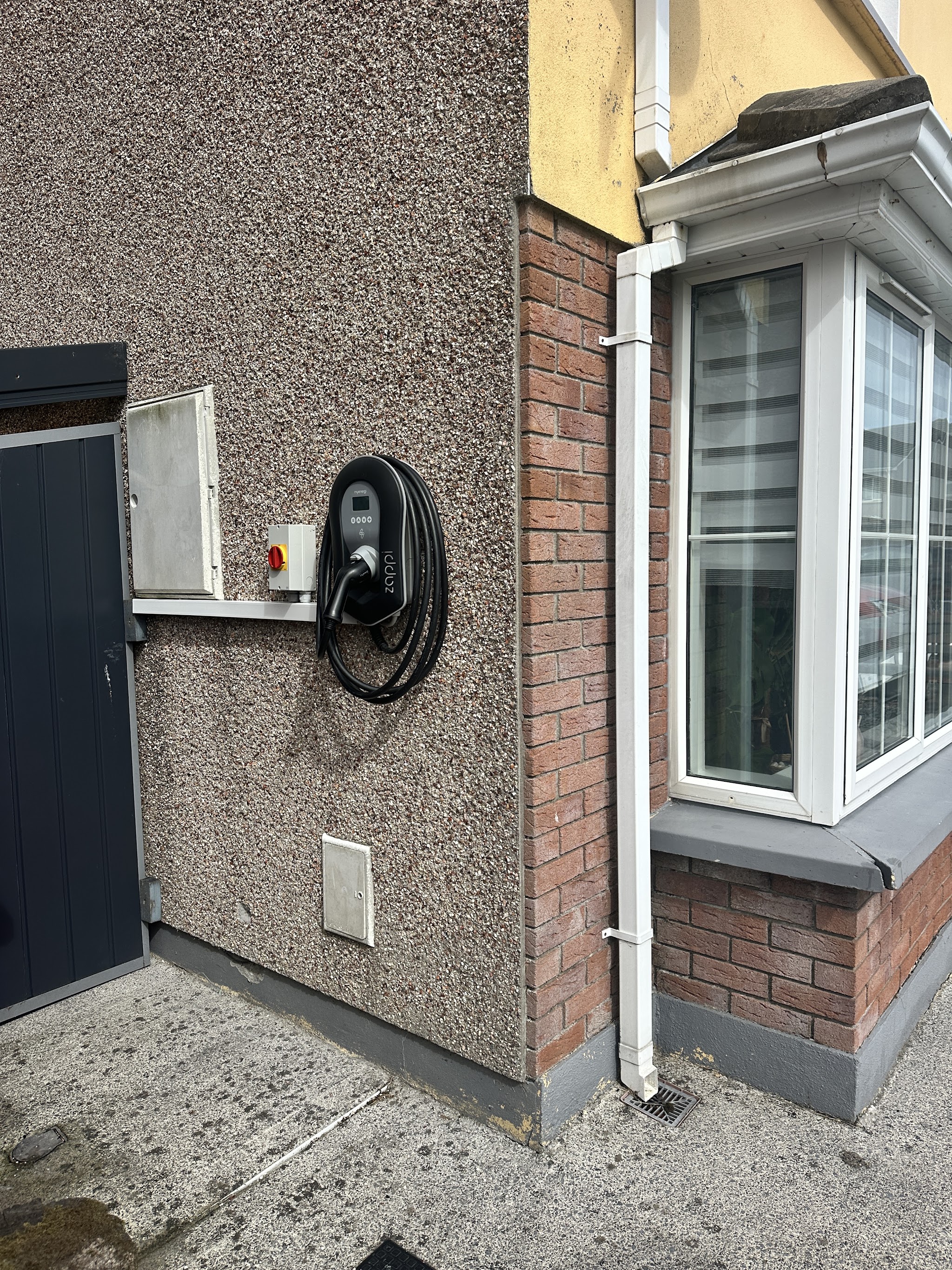 An EV charger on the side of a house, seen from the corner